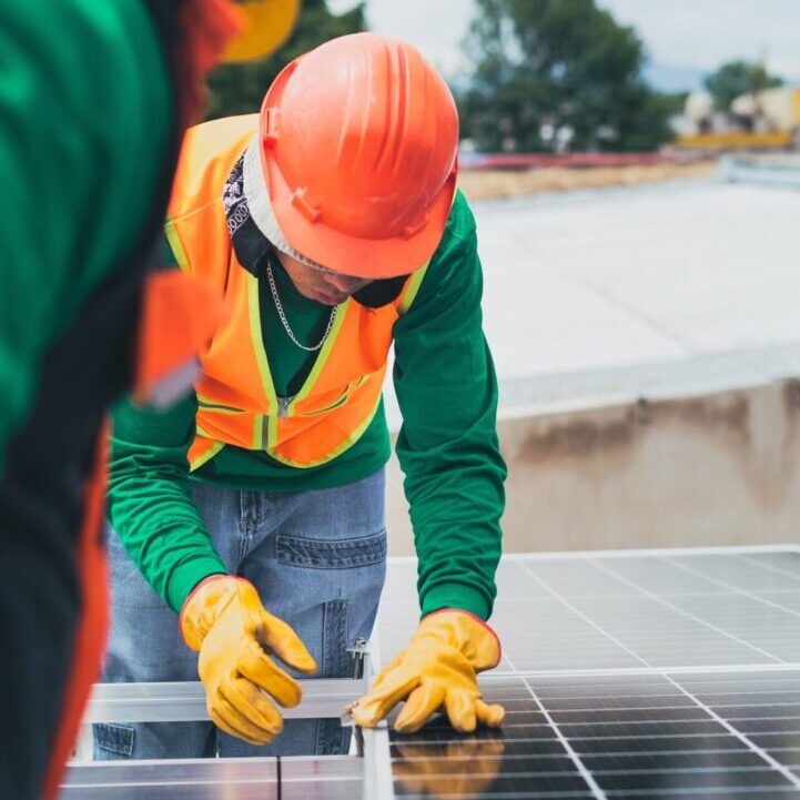 Worker installing solar panels wearing safety gear.